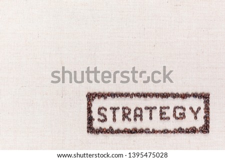 The word Strategy inside a rectangle written with coffee beans on creamy linea canvas, shot from above,aligned at the bottom right.