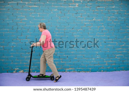 elderly woman in pink T-shirt and glasses is learning to ride new scooter. concept of an active lifestyle, sports