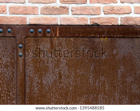 Surface of rusty metal with rivets and brick wall. Rust texture, background and pattern