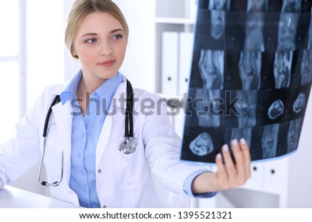 Doctor woman examining x-ray picture near window in hospital. Surgeon or orthopedist at work. Medicine and healthcare concept. Blue colored blouse of a therapist looks good