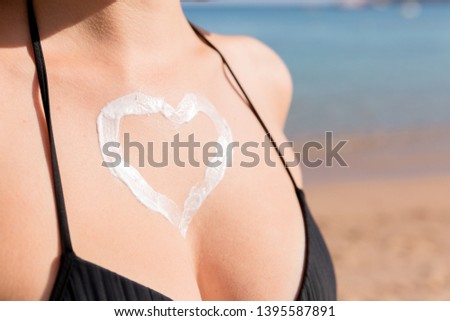 Tanned woman with heart shaped sun cream on her breast at the sea background.