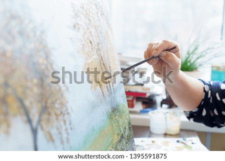 Female artist's hand in glove draws with an oil painting with a brush close-up, sunny day, horizontal