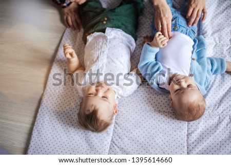 Two adorable twin brothers infant child baby toddler being caressed with parents lying on white carpet