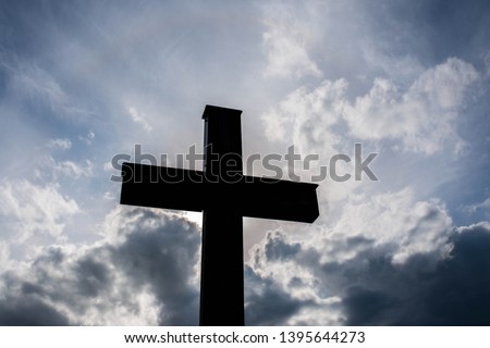 Simple wooden catholic cross silhouette, dramatic storm clouds on the sky.