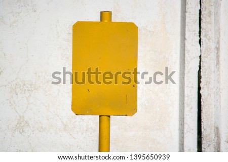 Yellow metal scoreboard (nameplate). Painted white. On the background - a concrete wall.