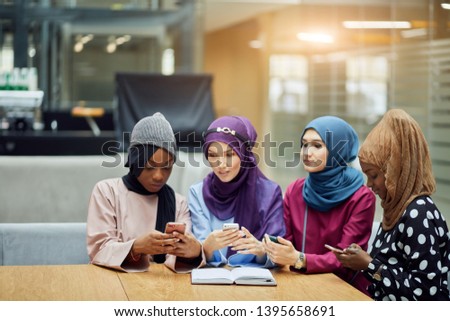 Islamic female travel blogger sharing info from smartphone with her followers while sitting in group of four in hotel lobby