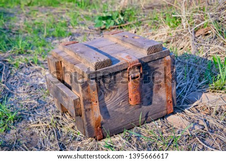 An antique wooden box with rusty metal hardware fittings rests on a grass background.
