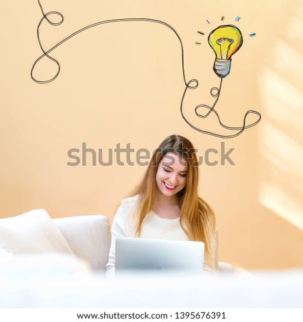 Light bulb with string with young woman using her laptop computer at home