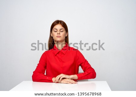 A woman in a red shirt is sitting at the white table indoors                        