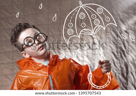 a boy in an orange raincoat and with a painted umbrella stands in the rain