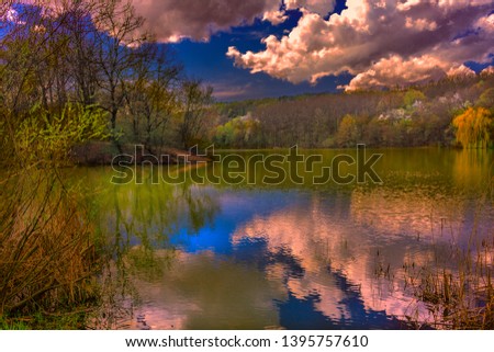 Quiet calm, serene silence over the beautiful mountain forest lake. Reflection of the sky and clouds in the water. The rays of the setting sun beautifully interesting and fascinating illuminate and il