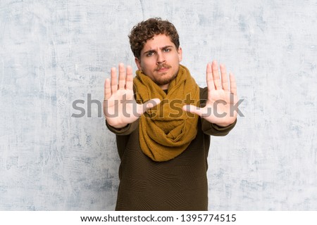 Blonde man over grunge wall making stop gesture and disappointed