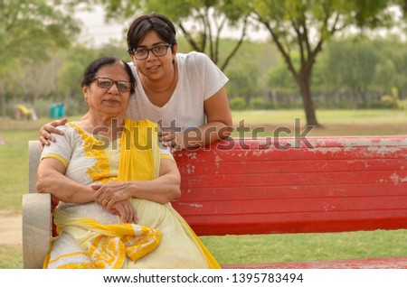 Happy looking young Indian woman with her mother sitting on a red bench in a park in New Delhi, India. Concept Mother's day