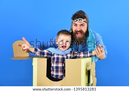 Little boy playing with handmade cardboard toy plane isolated on blue background. He dreaming of being a pilot. Father and son.