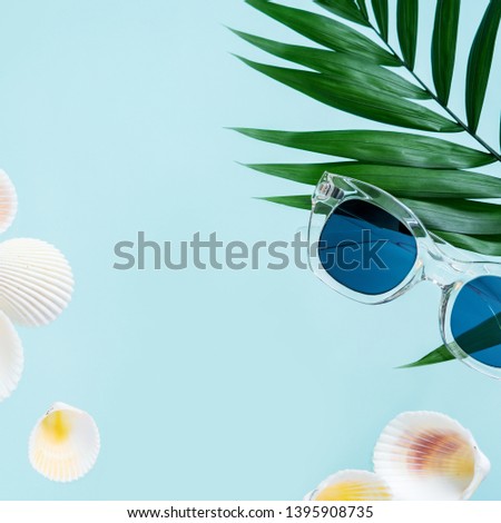 Summer creative concept. Minimal style with transparent sunglasses, palm leaves and seashells on turquoise background with copy space