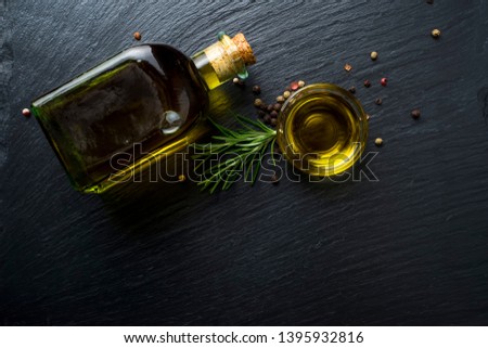 Virgin olive oil in a glass bottle, rosemary and peppercorns on black stone slate, top view with blank space. Royalty-Free Stock Photo #1395932816