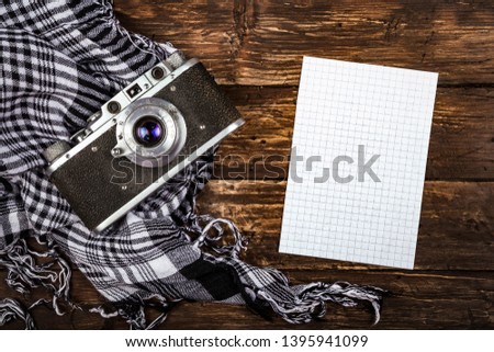 Old retro camera on vintage brown wooden board with black and white checkered scarf and piece of squared paper for notes. abstract background. Top view.Copy space for text.