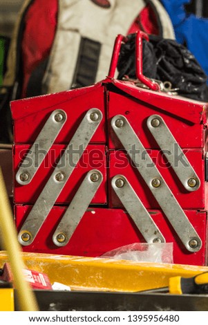 Bright red vintage retro style toolbox old and well used sat atop a steel workbench in a factory industrial area.Used on many machines and equipment for international trade and commerce from the start