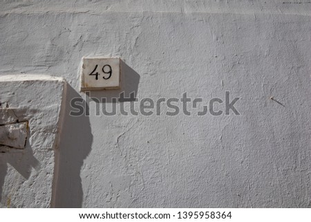 White house street number forty-nine 49 carved into marble parallelepiped full with black paint, white-washed buildings in Noci, Puglia, Italy with summer day shadows