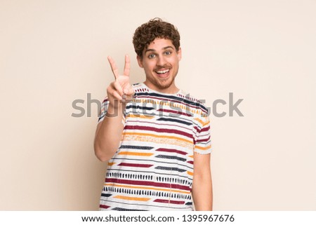 Blonde man over isolated wall smiling and showing victory sign