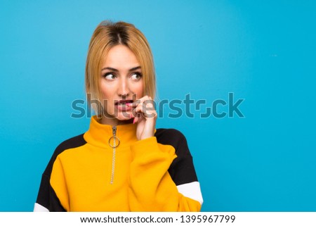Young blonde woman over isolated blue background nervous and scared