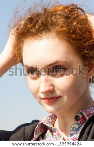 Red-haired young girl on a background of clear blue sky