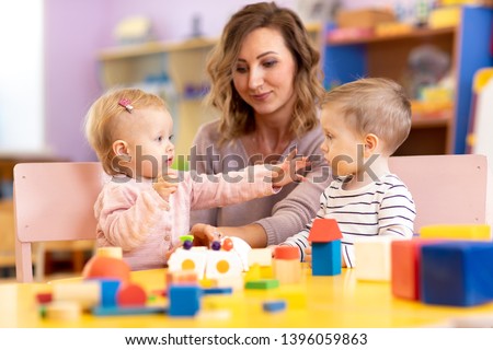 Babies with mentor in kindergarten. Kids toddlers in nursery school. Little girl and boy preschoolers playing with teacher. Royalty-Free Stock Photo #1396059863