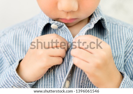 Child Development concept: Close up of a little kindergarten boy's hands learning to get dressed, buttoning his striped blue shirt. Montessori practical life skills - Care of self, Early Education. Royalty-Free Stock Photo #1396061546
