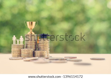 Saving for child education, financial concept : Golden trophy cup, black graduation cap, family members with a kid on rows of rising coins, depict money or asset arrangement for learning and knowledge