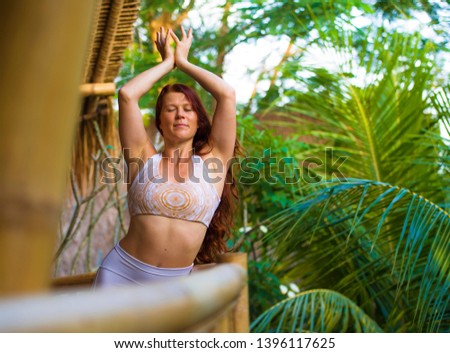 natural portrait of young happy and attractive woman with beautiful long red hair doing yoga meditation exercise at amazing tropical jungle background in healthy lifestyle and harmony