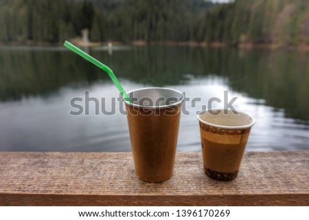 Two paper cups are on the parapet. In the background is a lake with turquoise water.