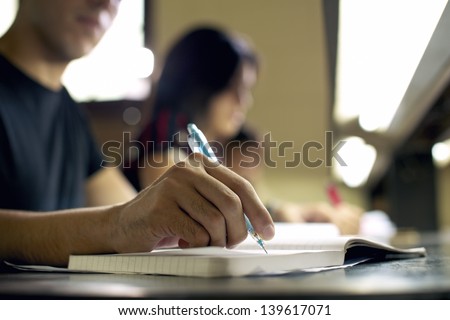 Students doing homework and preparing exam at university, closeup of young man writing in college library