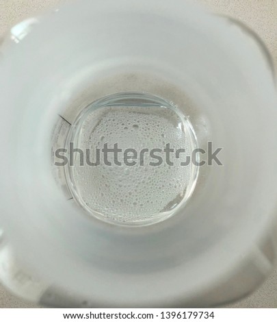 Top view through circular bottle neck of saline water with small bubbles on the surface inside clear plastic bottle
