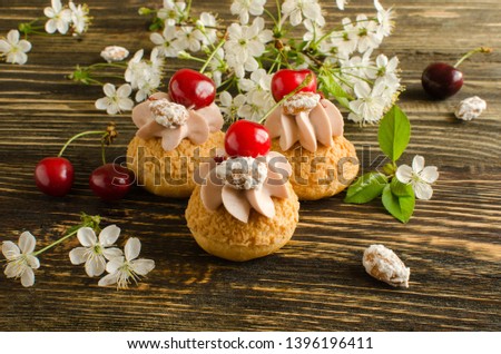 Choux Buns with Craquelin (crispy cream puffs) filled with cherry cream decorated with fresh cherry, cherry flowers and almonds on wooden background