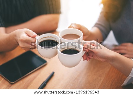 Top view image of three people clinking coffee cups on wooden table in cafe