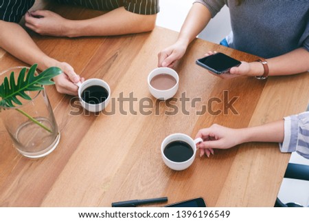 Top view image of three people holding coffee cups to drink on wooden table