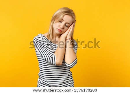 Relaxed young woman in striped clothes sleeping with folded hands under cheek isolated on yellow orange wall background in studio. People sincere emotions, lifestyle concept. Mock up copy space