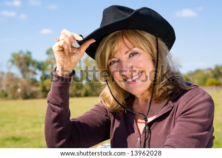 Beautiful mature woman tipping her cowboy hat on a farm.