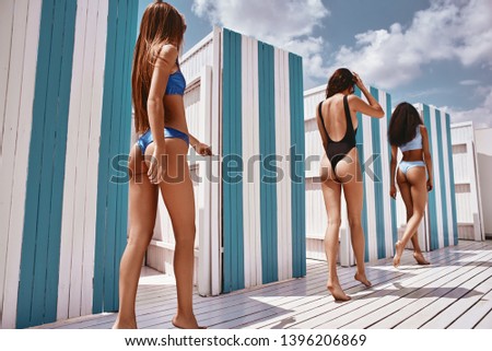 Don’t sit to be fit. Girls standing near changing booths on the beach