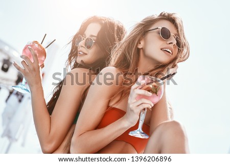 Summer fun has begun. Girls sitting by the pool, drinking cocktails