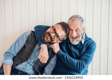 A portrait of adult hipster son and senior father sitting on floor indoors at home. Royalty-Free Stock Photo #1396218905