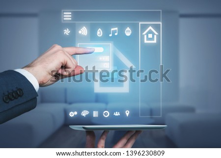 Man hand holding digital tablet with smart home hologram over blurred living room background. Concept of IoT and hi tech. Toned image double exposure