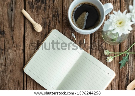 Black coffee cup with white flower& blank notebook on wooden table. The morning light from window makes the house more cozy& romantic. This photo is good for chillout music cover. Lazy Sunday concept.