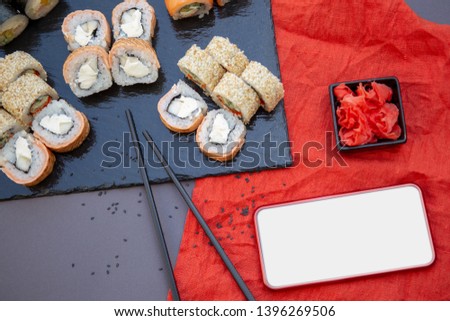 Smartphone with empty screen, chinese sushi roll, soy sauce, sticks,  on red background with copy space. Online food delivery concept. Top view, flat lay. Mobile phone mockup.