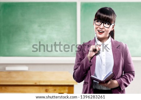 Asian student woman with notebook and pen thinking something in the classroom with chalkboard background. Back to School concept