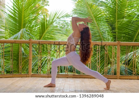 outdoors natural portrait of young beautiful and happy red hair woman doing yoga at tropical fitness studio practicing balance and concentration with jungle background in healthy lifestyle concept