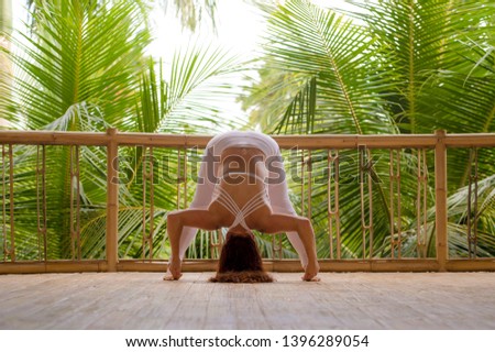 outdoors natural portrait of young attractive and happy red hair woman doing yoga at tropical fitness studio practicing balance and concentration with jungle background in healthy lifestyle concept