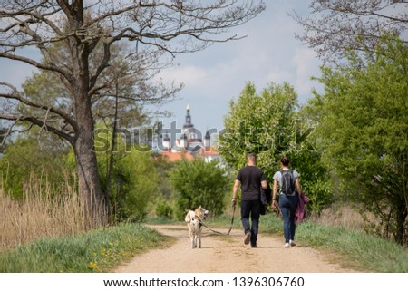 man and woman walk the dog along the river against the backdrop of the monastery in Supral, Poland. The concept of spending holidays in the era of coronavirus.