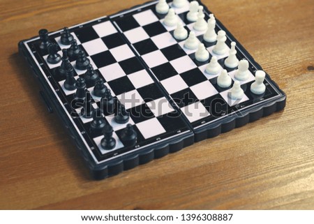 Foldable plastic chessboard with black and white chess on a wooden surface. Top view