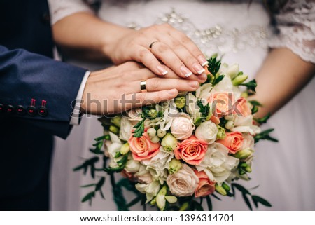 hands of the bride and groom with gold wedding rings on them, lie on a wedding bouquet with fresh flowers